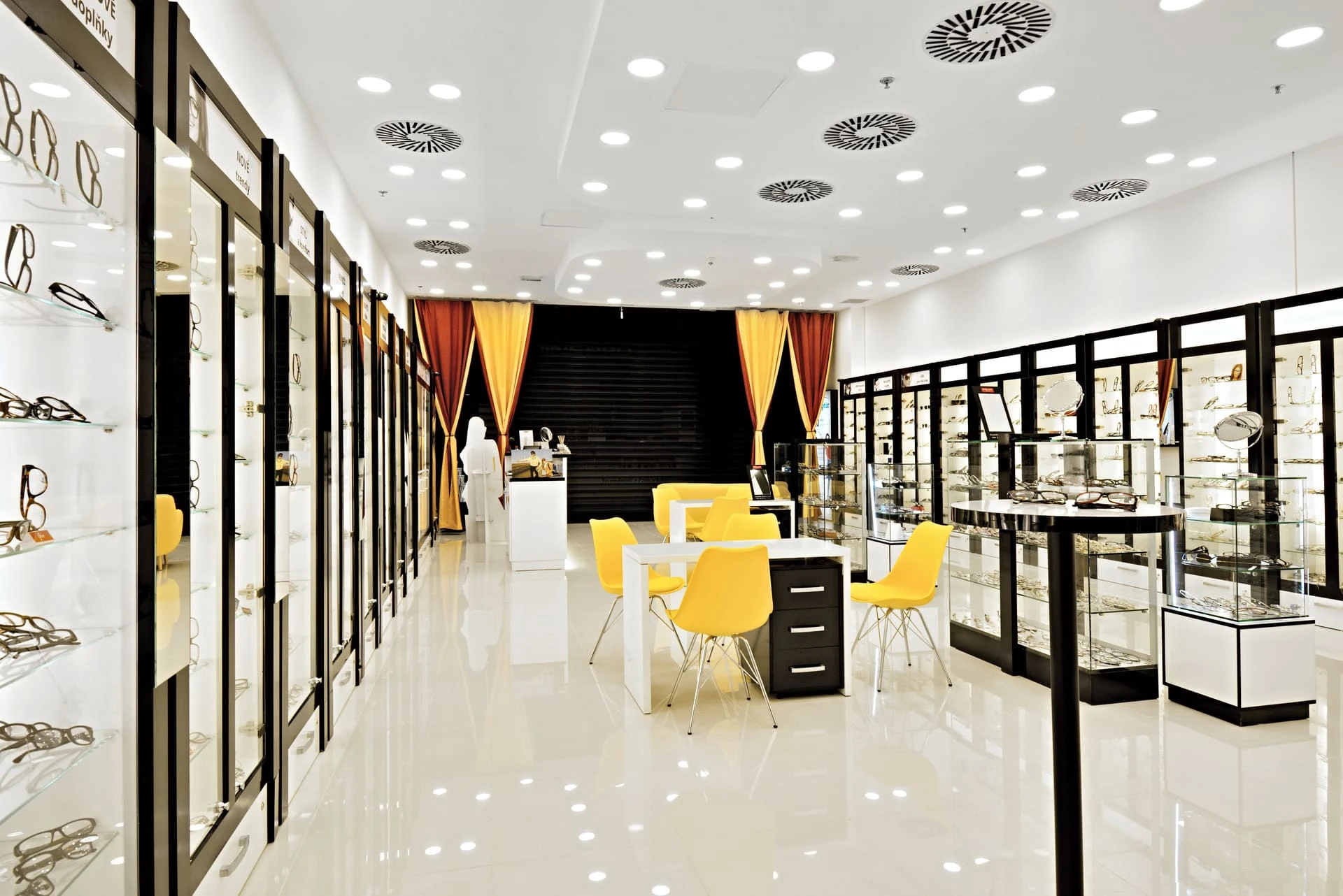 Vitríny s brýlemi, uprostřed místnosti stolek se žlutými židlemi