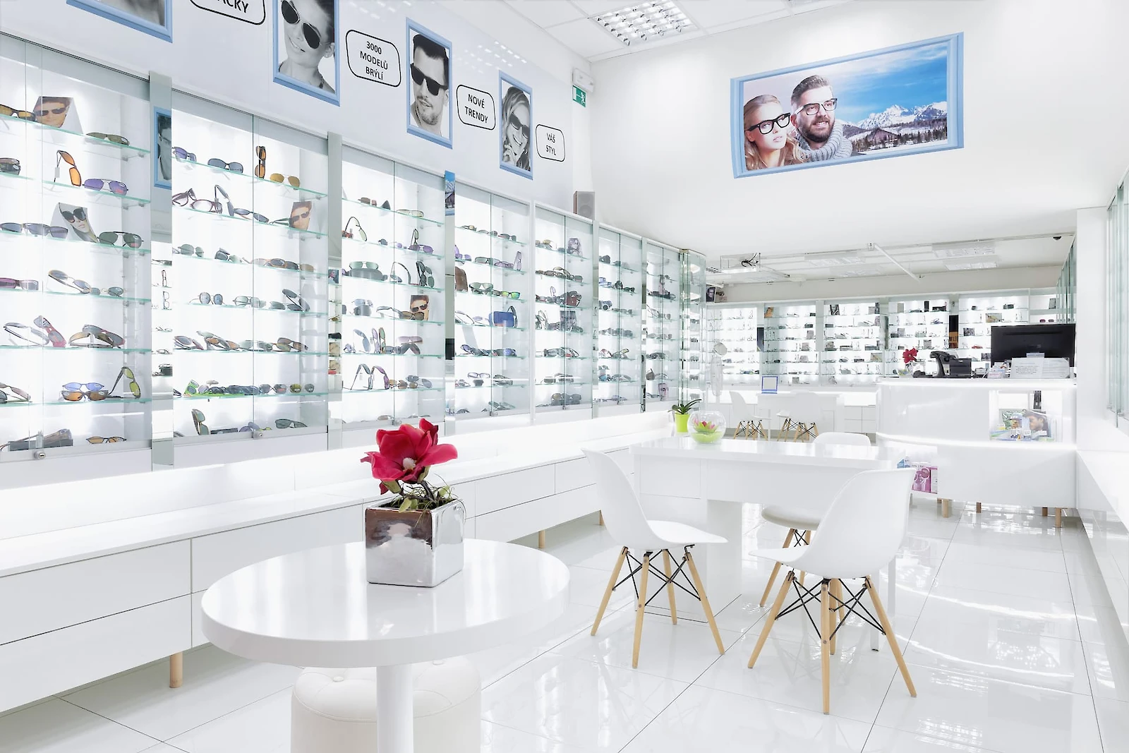 Vitríny s brýlemi, bílý stolek a bílé židle