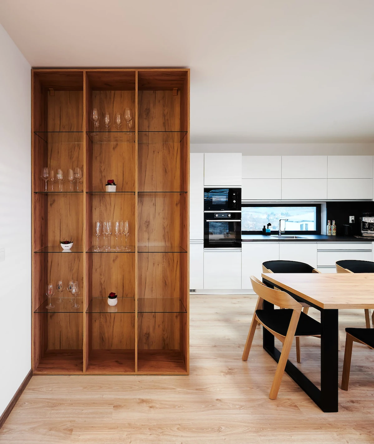 Dřevěná skříň se skleněnými policemi, průhled do kuchyně a jídelny