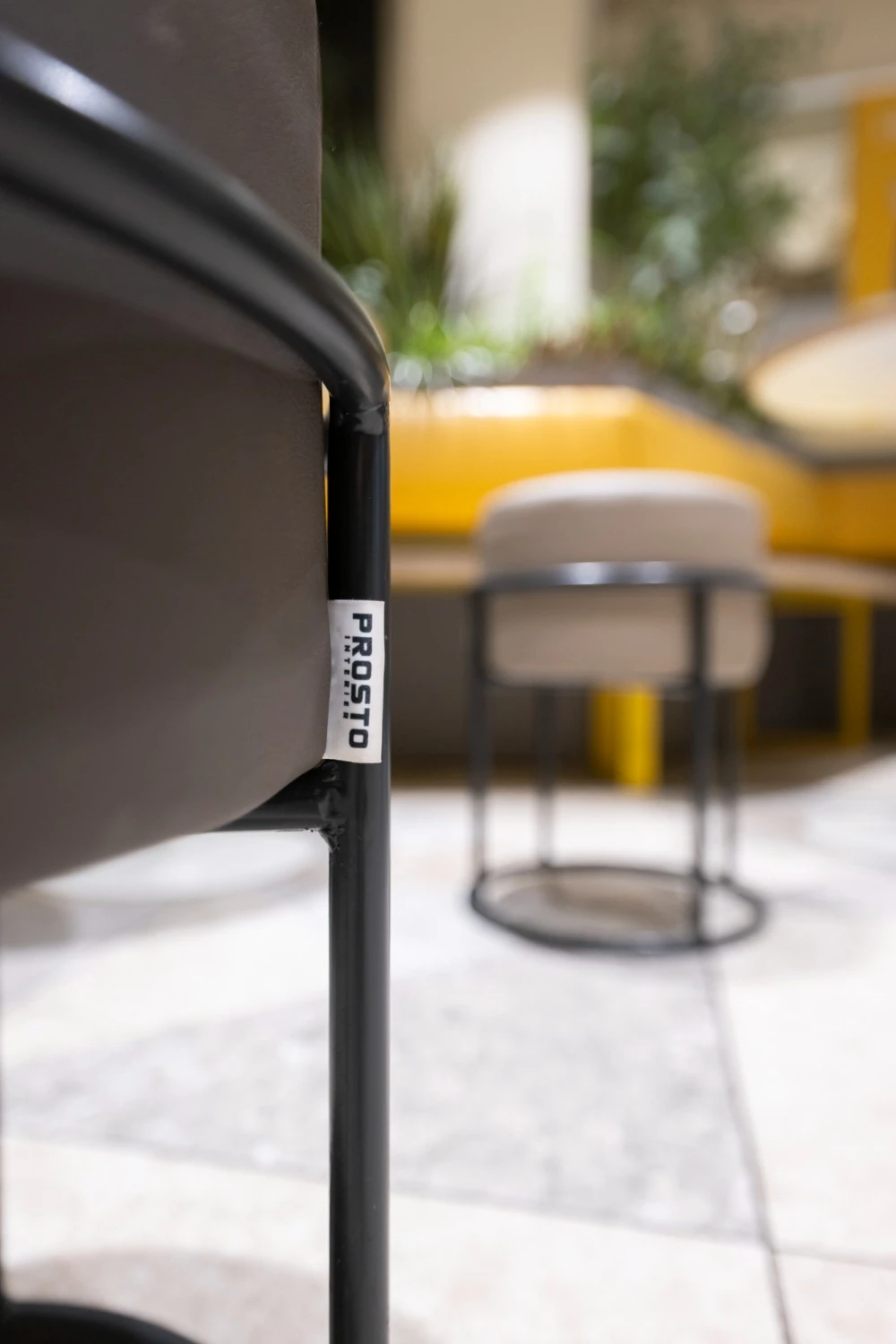 Detail stolu s kelímkem a žlutou židlí, v pozadí interiér restaurace